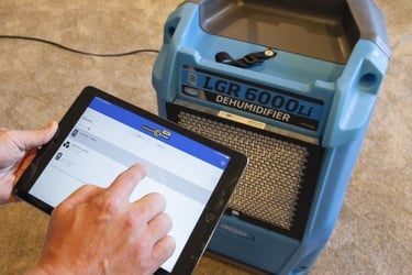 A hand looking at a tablet that is connected to LGR 6000li dehumidifier