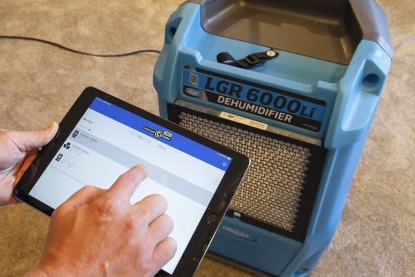 A hand looking at a tablet that is connected to LGR 6000li dehumidifier