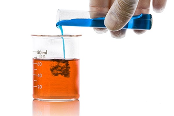 Blue liquid from a vial being poured into a beaker with orange liquid in it. 