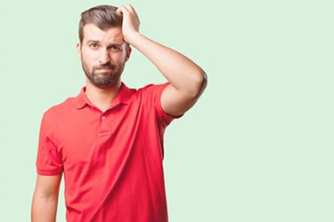 Man in red shirt looking upset holding his head. 