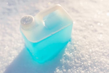 Blue liquid chemical in a clear container on snow. 