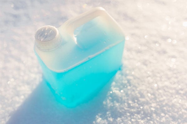 Blue liquid chemical in a clear container on snow. 