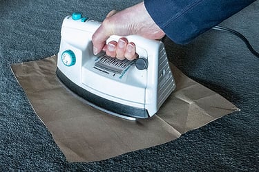 Hand holding an iron with a butcher paper attempting to take wax out of a carpet. 