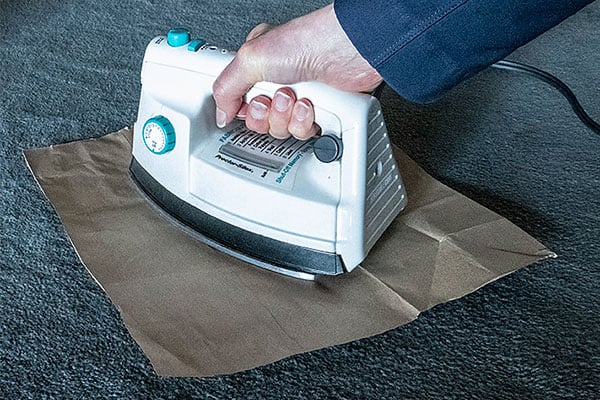 Hand holding an iron with a butcher paper attempting to take wax out of a carpet. 