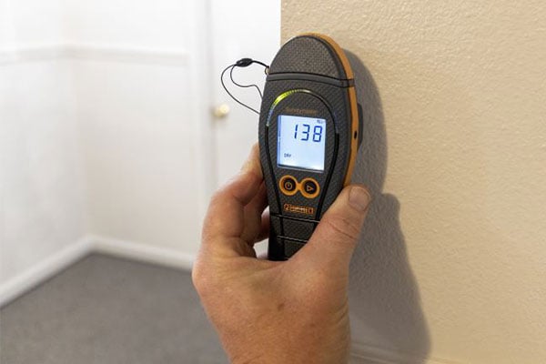 Hand holding a moisture meter against a wall. It reads 138.
