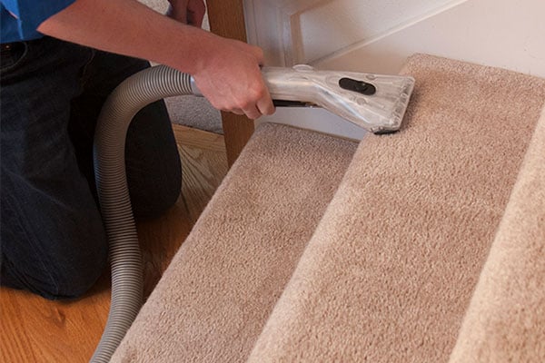A persons hand using a cleaning carpet wand on stairs. 