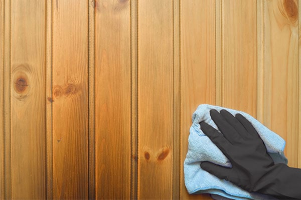 Gloved hand using a towel to wipe down a wood wall. 