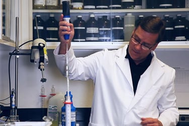 Male scientist putting a large plastic needle into a tube.