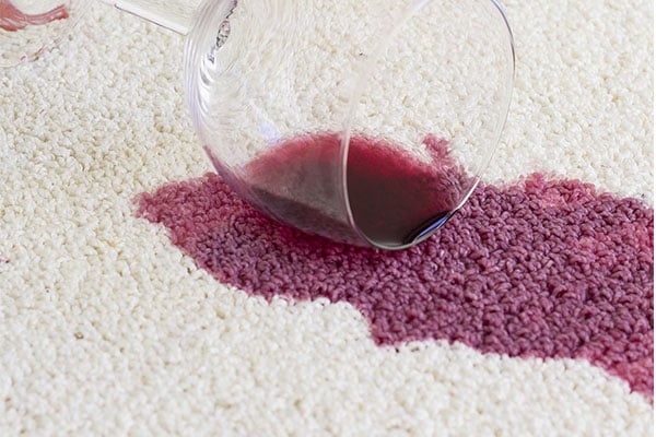 Spilled red wine staining a white carpet. 
